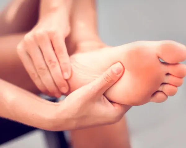 Hands massaging a foot, seeking aching feet remedy. The sole of the foot shows a slight red hue, indicating discomfort.