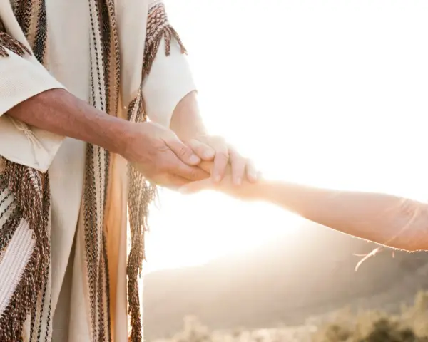 A person in a robe holds another's hand, symbolizing how to surrender to God through trust and guidance.