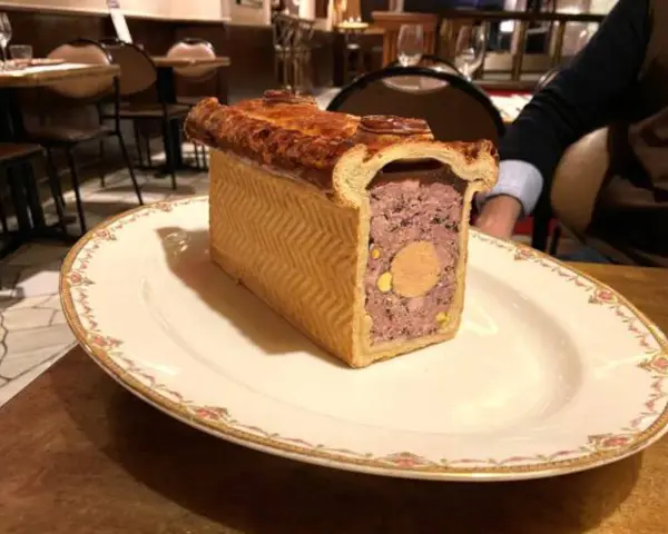 Un delicioso pâté de paques, un pastel de carne con un centro de foie gras, servido en un plato elegante.