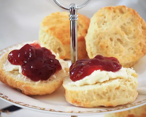 Was sind Scones? Köstliche, goldbraune Scones, bestrichen mit Clotted Cream und Marmelade, auf einer Etagere serviert. Ein Genuss für jeden Teeliebhaber.