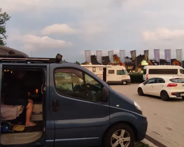 Na parkingu przy Chochołowskich Termach stoi ciemnoniebieski bus, biały samochód i kamper.