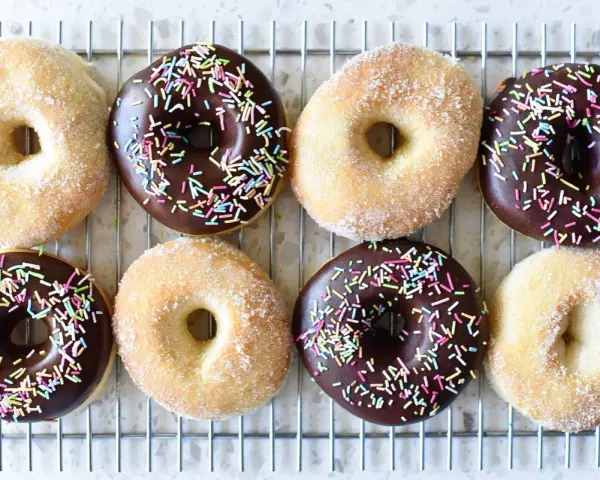 Åtta hemgjorda donuts, vissa med chokladglasyr och strössel, andra med socker. Perfekt för ett donuts recept!