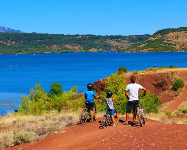 Famille à vélo profitant d'une randonnée au lac du Salagou, avec ses eaux bleues et ses collines rouges.