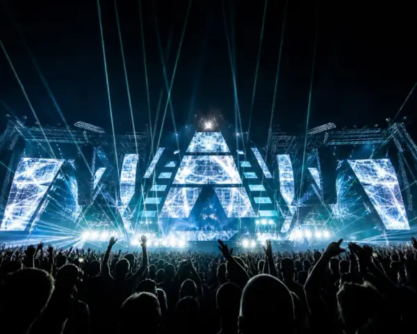 Eine riesige Menge jubelt bei einem EDM-Konzert. Die Bühne ist mit geometrischen Mustern und blauen Lichtern beleuchtet, was die Bedeutung von EDM-Musik für die Fans unterstreicht.