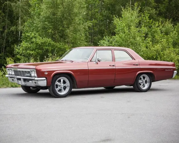 Röd Chevrolet Impala från 1965 med en tung cut, parkerad vid en skogsdunge.