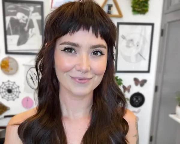 Uśmiechnięta kobieta z ciemnymi włosami i grzywką baby bangs.