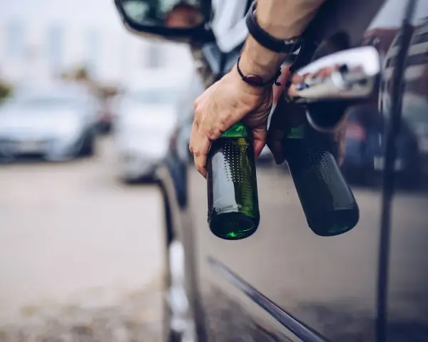 Mann hält zwei Bierflaschen aus dem Autofenster. Er versucht, den Alkohol abzubauen, indem er sie wegwirft.