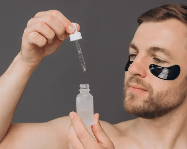 Homme avec patchs oculaires noirs appliquant un sérum. Découvrez les acide glycolique bienfaits pour une peau éclatante.