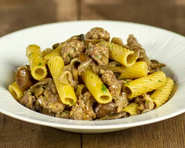 Piatto di pasta funghi e salsiccia, con rigatoni conditi con funghi trifolati e pezzetti di salsiccia saporita.