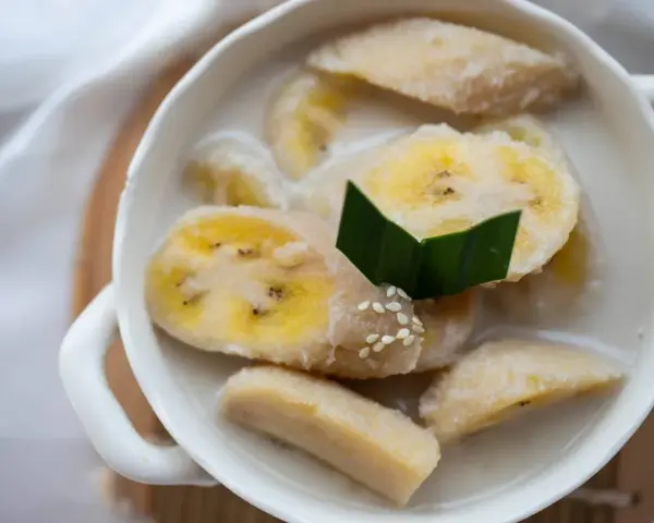 Kawałki banana w mleku kokosowym, ozdobione liściem pandanu i sezamem. Pyszny tajski deser.