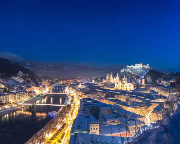 Magiczne salzburg zimą. Oświetlone miasto, rzeka Salzach i górująca twierdza Hohensalzburg w śnieżnej scenerii nocą.