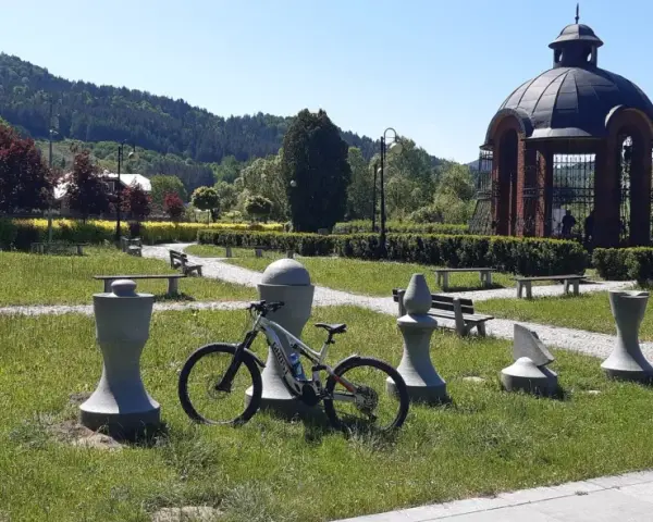 Rower czeka na ścieżce w Piwnicznej-Zdroju, wśród kamiennych figur i zieleni.