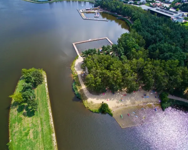 Widok z lotu ptaka na jezioro z kąpieliskiem, plażą i lasem.