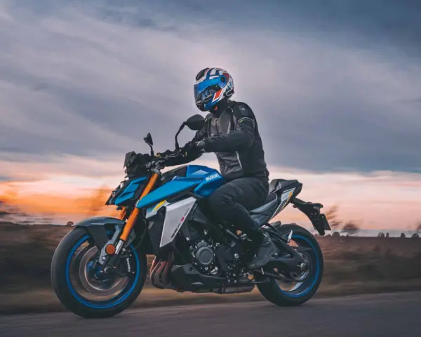 Motocyklista w kasku jedzie na niebieskim Suzuki GSX-S1000 podczas zachodu słońca.