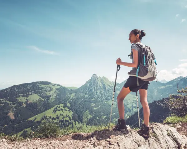Dziewczyna z plecakiem i kijkami do trekkingu podziwia górski krajobraz. To jest właśnie hiking – przygoda na łonie natury.