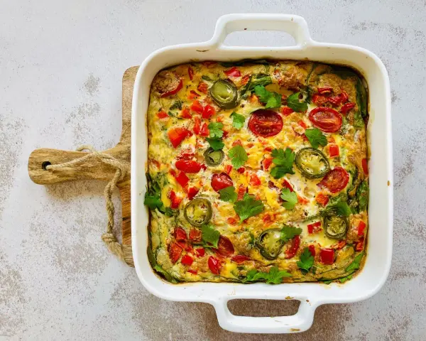 Pyszny omlet z piekarnika z pomidorkami, papryką i jalapeño, udekorowany natką pietruszki.