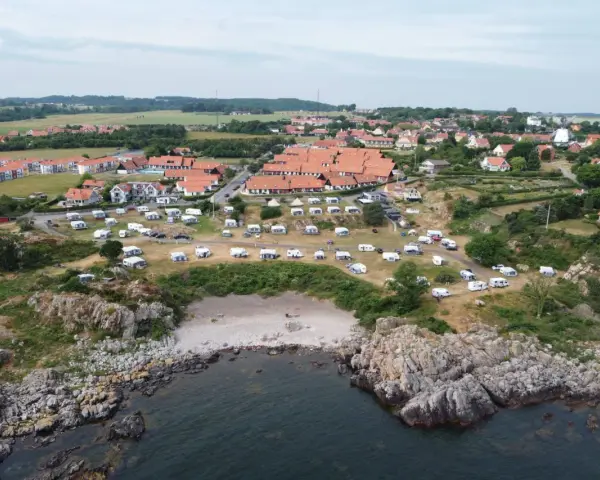 Sannes familjecamping vid kusten, med husvagnar och tält utspridda bland klippor och grönska.