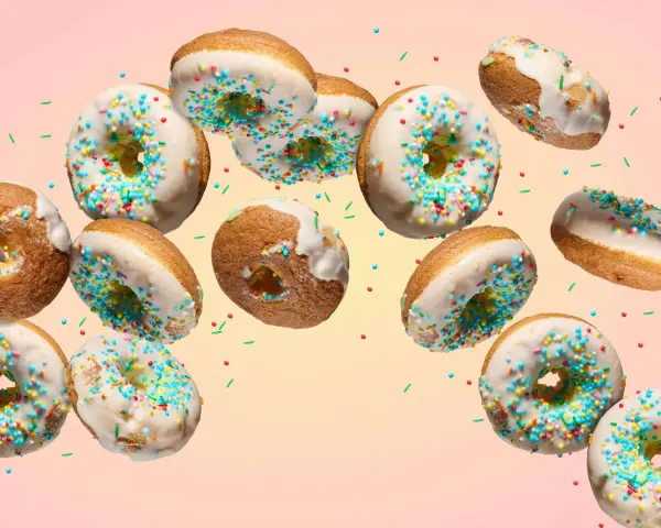 Bunte Donuts mit weißer Glasur und Streuseln schweben im Bild. Ein köstliches Rezept für selbstgemachte Donuts.