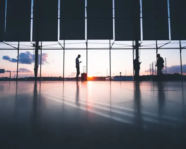 Sylwetki ludzi z bagażami czekają na lotnisku o zachodzie słońca. Czyżby to był kolejny przypadek overbookingu Ryanair?