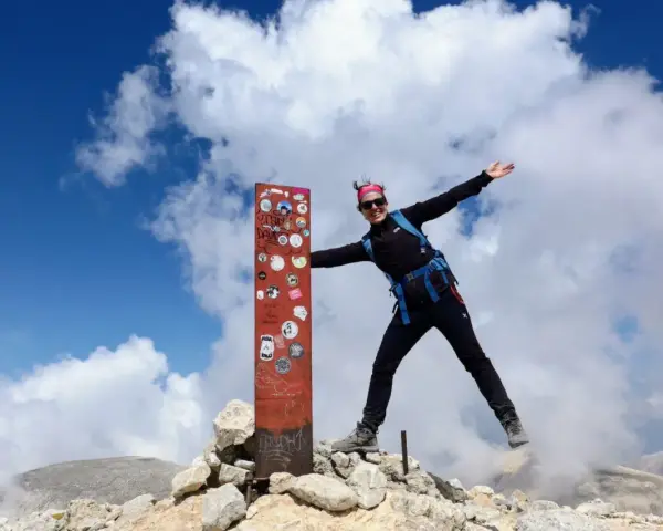 Donna esulta in cima al Monte Amaro dopo un trekking. Cielo azzurro e nuvole bianche.
