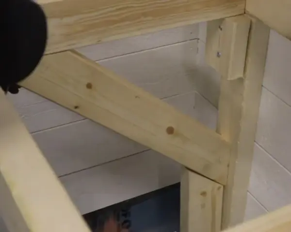 En person håller på att såga snett en träbit som ska bli en del av en konstruktion.