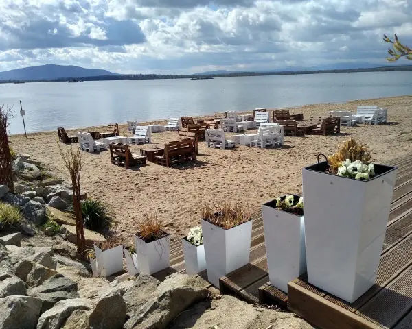 Plaża nad mietkowym zalewem z meblami z palet. W oddali góra i jezioro.