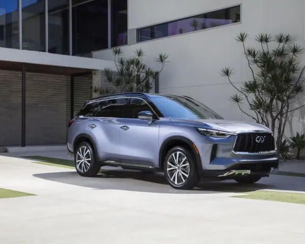 Elegancki, srebrny infiniti samochód zaparkowany przed nowoczesnym budynkiem z kamienną fasadą i dużymi oknami.