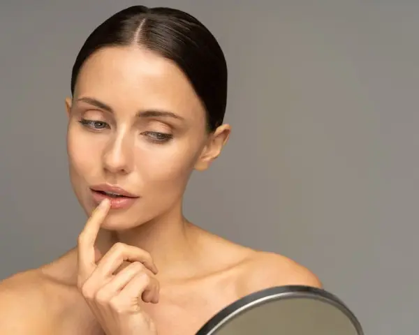 Mujer se toca los labios con el dedo, reflexionando sobre cómo hidratar los labios para una piel radiante.
