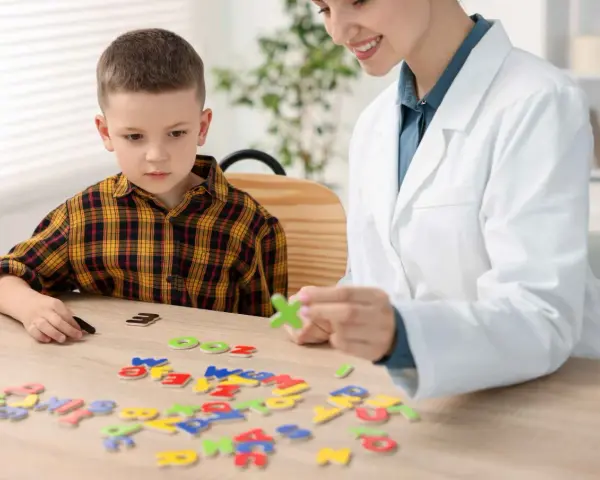 Chłopiec z dysleksją układa litery z terapeutką. Czy dysleksja to choroba? Terapia pomaga w nauce.