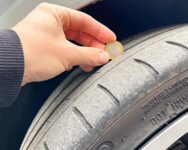 Una mano tiene una moneta da 1 euro per mostrare quanti mm di battistrada ha un pneumatico nuovo. Il battistrada è usurato.