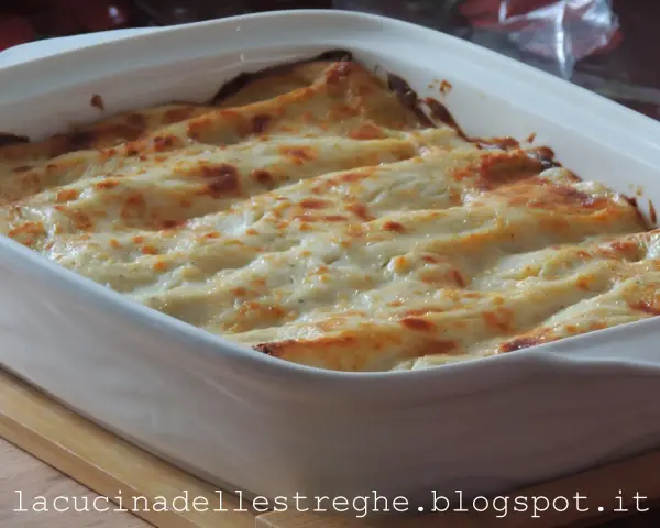 Lasagne con carciofi, besciamella e mozzarella appena sfornate, dorate e filanti in una teglia bianca.