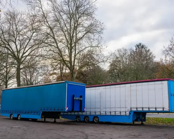 Dwa naczepy ciężarowe, jedna niebieska, druga biała, stoją obok siebie. Symbolizują one dynamiczną branżę TSL.