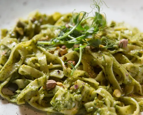 Makaron tagliatelle z zielonym sosem pesto, posypany pistacjami i udekorowany kiełkami.