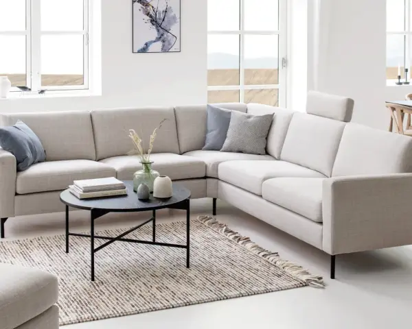 Inspiration kuddar till grå soffa: en ljusgrå hörsoffa med blå och grå mönstrade kuddar, ett runt svart soffbord med böcker och vaser, samt en randig matta.
