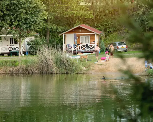 Rodzina odpoczywa nad jeziorem w malowniczym miejscu. Dzieci pluskają się w wodzie, a dorośli relaksują się na plaży przy domkach kempingowych. To idealne miejsce na rodzinne wakacje, prawdziwa **camping forteca** spokoju i radości.