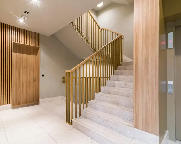 Nowoczesna klatka schodowa z drewnianą okładziną i złotymi balustradami. Osłona ściany przy schodach podkreśla elegancję wnętrza.