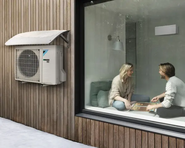 Unidad exterior de aire acondicionado Daikin instalada bajo un alero protector en una pared de madera. Ideal para saber donde colocar la unidad exterior del aire acondicionado.