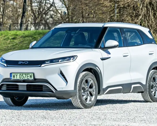 Biały SUV z logo BYD, jeden z chińskich samochodów elektrycznych, zaparkowany na żwirowej nawierzchni.