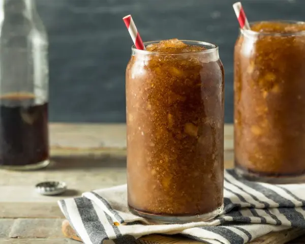 Zwei Gläser mit erfrischendem Cola Slush Eis, bereit zum Genießen. Eine Flasche Cola steht daneben.