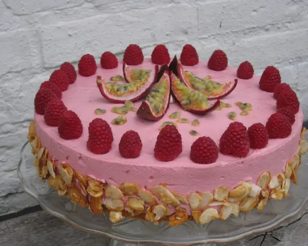 En rosa hallonmousse tårta dekorerad med färska hallon och passionsfrukt. Kanterna är täckta med rostade mandelflagor.