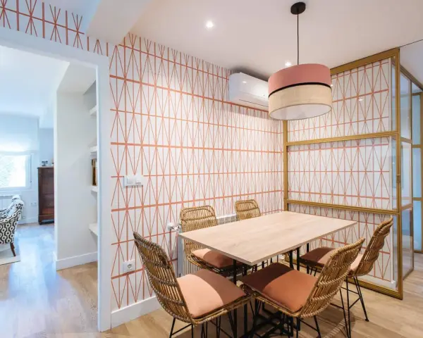 Comedor con pared empapelada con un diseño geométrico en naranja. Mesa de madera con sillas de ratán y cojines terracota.