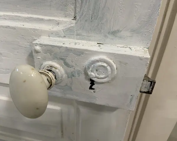 Poignée de porte ancienne recouverte de peinture blanche écaillée, prête à être nettoyée.