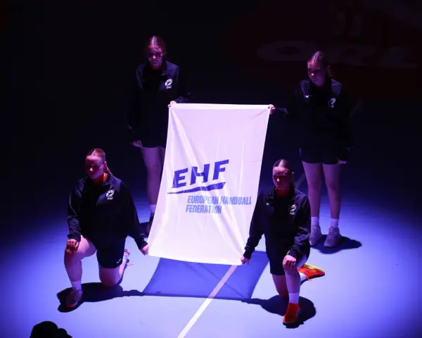 Cztery młode kobiety prezentują flagę EHF przed meczem ligi mistrzów w piłce ręcznej mężczyzn.