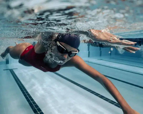 Une femme en maillot de bain rouge nage en crawl, lunettes de natation sur le nez. Sa **natation transformation physique femme** est visible sous l'eau.