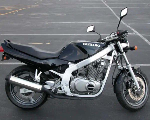 Czarny motocykl Suzuki GS 500 z chromowanym wydechem stoi na pustym parkingu.