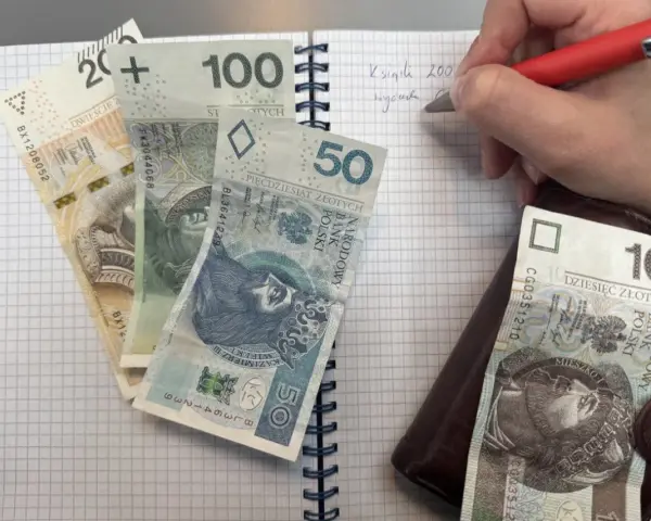 Zapisywanie wydatków na dziecko z orzeczeniem o potrzebie kształcenia specjalnego. Na zeszycie leżą banknoty 200, 100, 50 i 10 zł.
