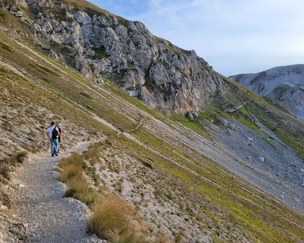 Due escursionisti percorrono un sentiero di trekking sul Gran Sasso, tra rocce e vegetazione alpina.