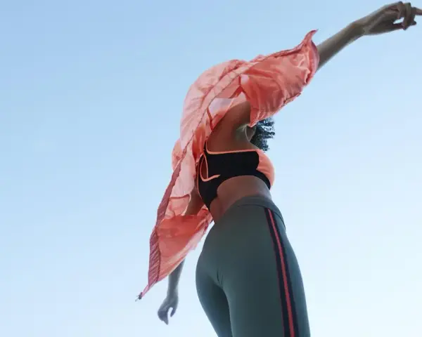 Kobieta w sportowym stroju, w tym legginsach z materiału spandex, tańczy na tle błękitnego nieba.