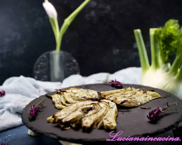 Finocchi croccanti e dorati, cotti nella friggitrice ad aria, serviti su una pietra scura con erbe aromatiche.
