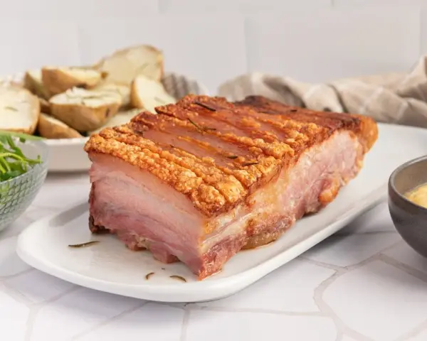 Panceta de cerdo al horno con piel crujiente, acompañada de patatas asadas y ensalada.